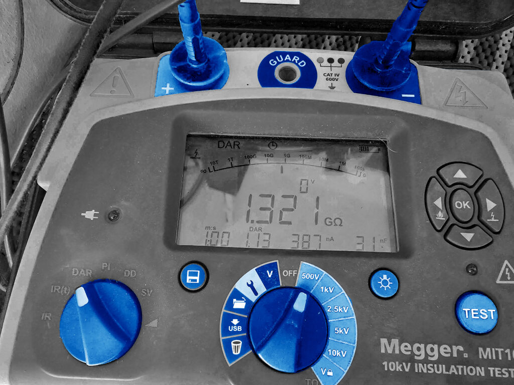 Megger Isolationsmessgerät zeigt Messwert von 1,321 GΩ, blaue Messleitungen an GUARD‑ und Plus‑Anschlüssen verbunden,