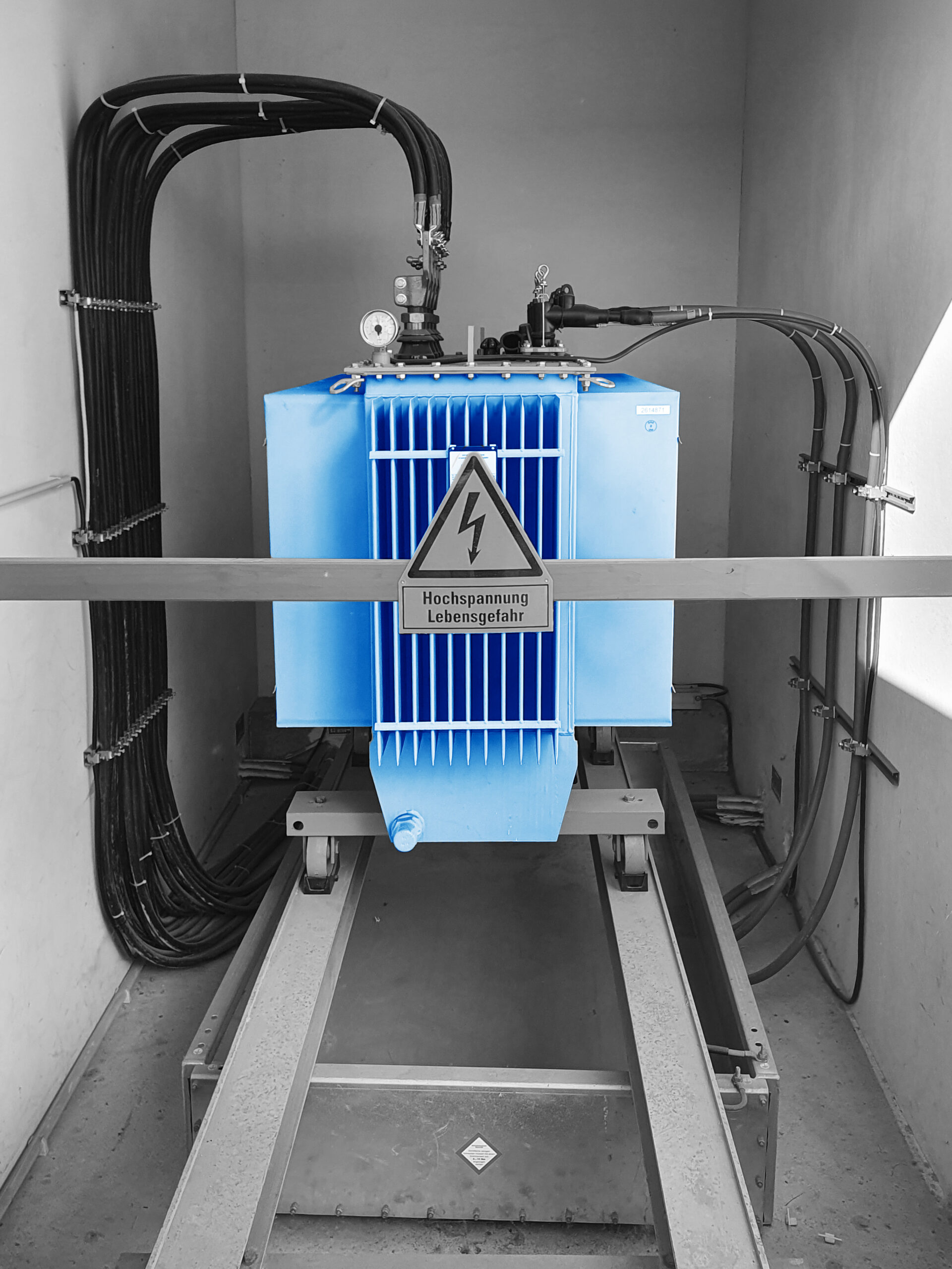 Blauer Transformator in Betonkammer mit angeschlossenen Hochspannungskabeln.