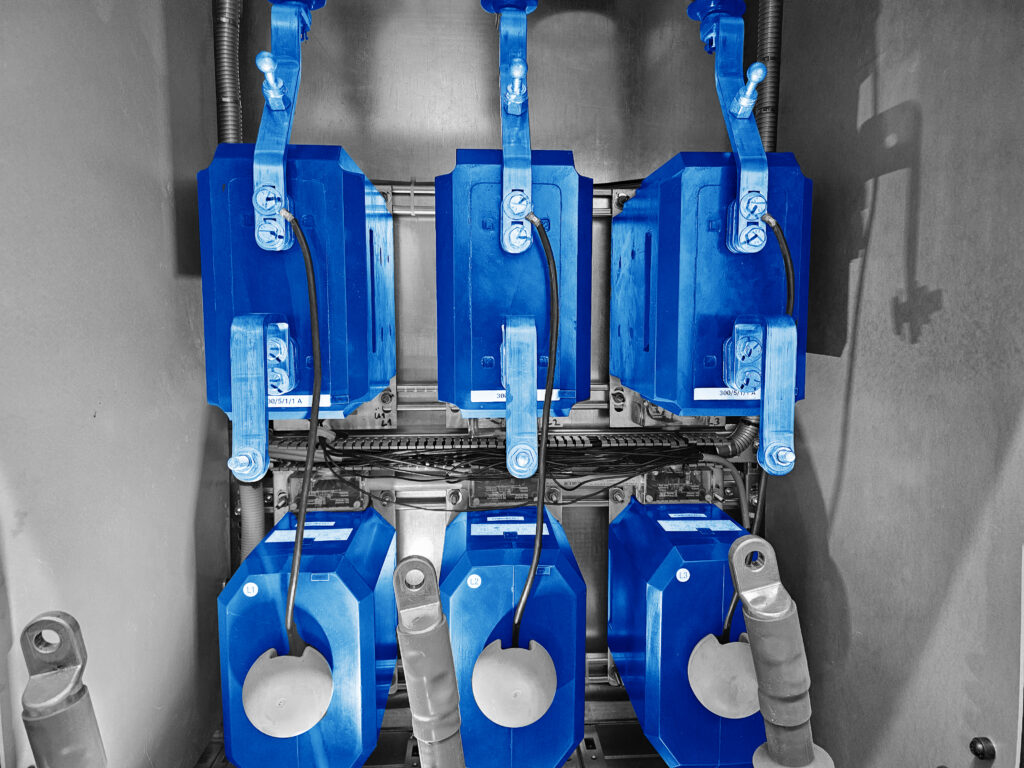 Blaue Mittelspannungs‑Stromwandler in geöffneter Schaltanlage, Messleitungen angeschlossen.