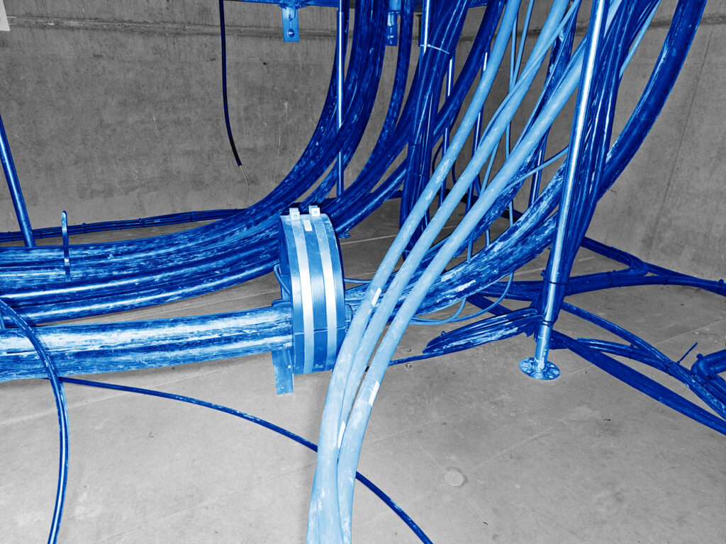 Mehrere blaue Kabel und Leitungen  verlaufen gebündelt durch einen  Betonkanal.