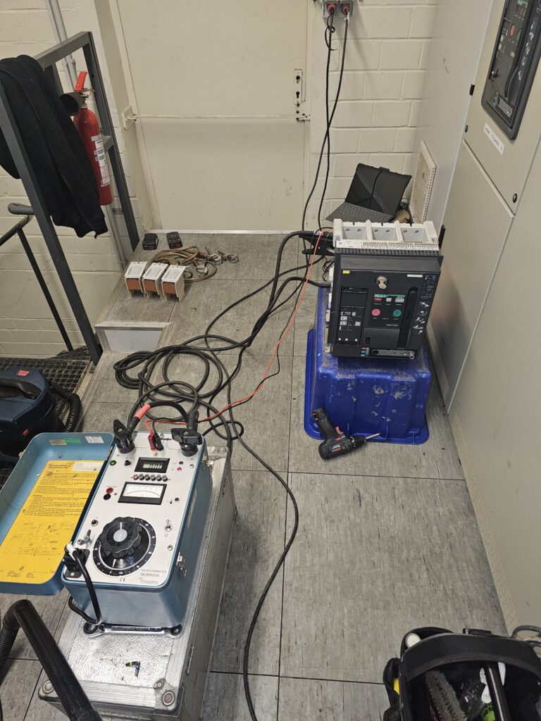 Messgeräte und Leistungsschalter stehen in Technikraum zur Funktionsprüfung und Wartung einer Trafoanlage, mehrere Kabel verbunden.