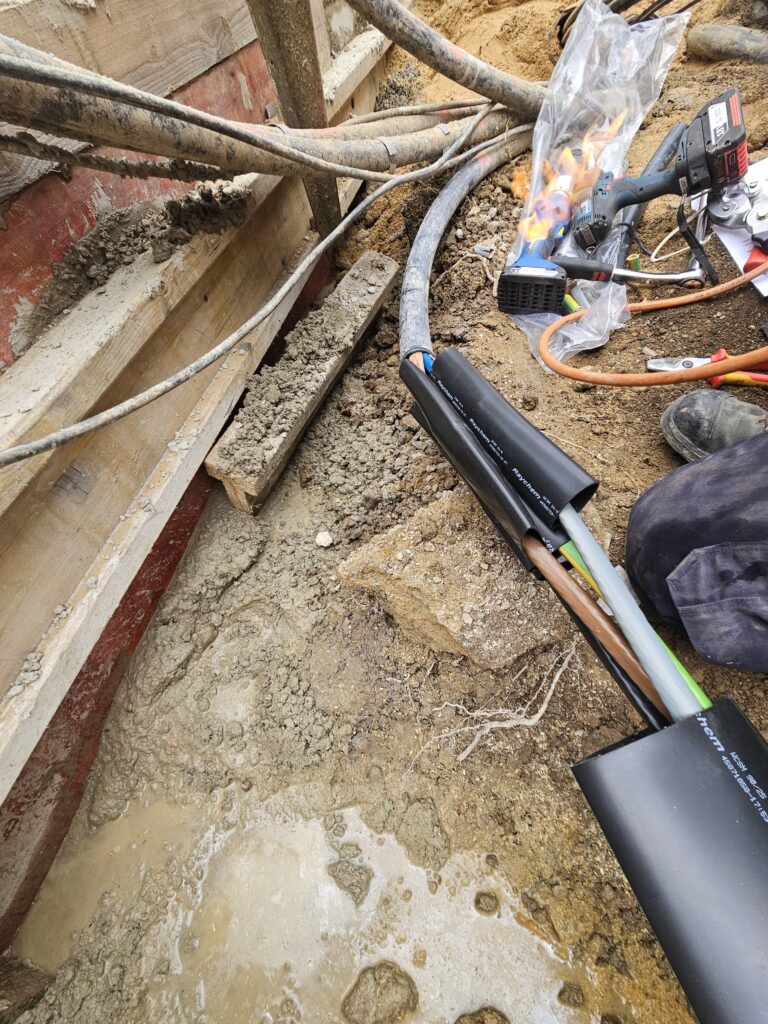Offene Stromkabel werden mit Schrumpfmuffen verbunden bei Erdarbeiten auf Baustelle.