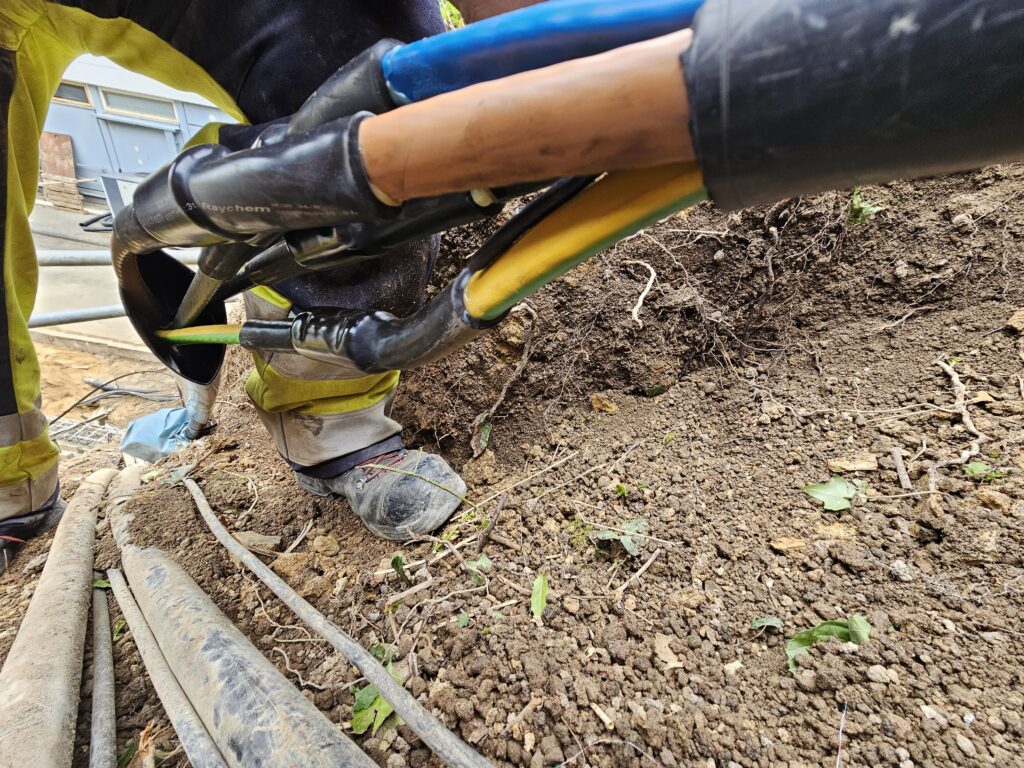 Monteure verbinden Stromkabel mit Schrumpfmuffen im Erdreich bei Bauarbeiten.