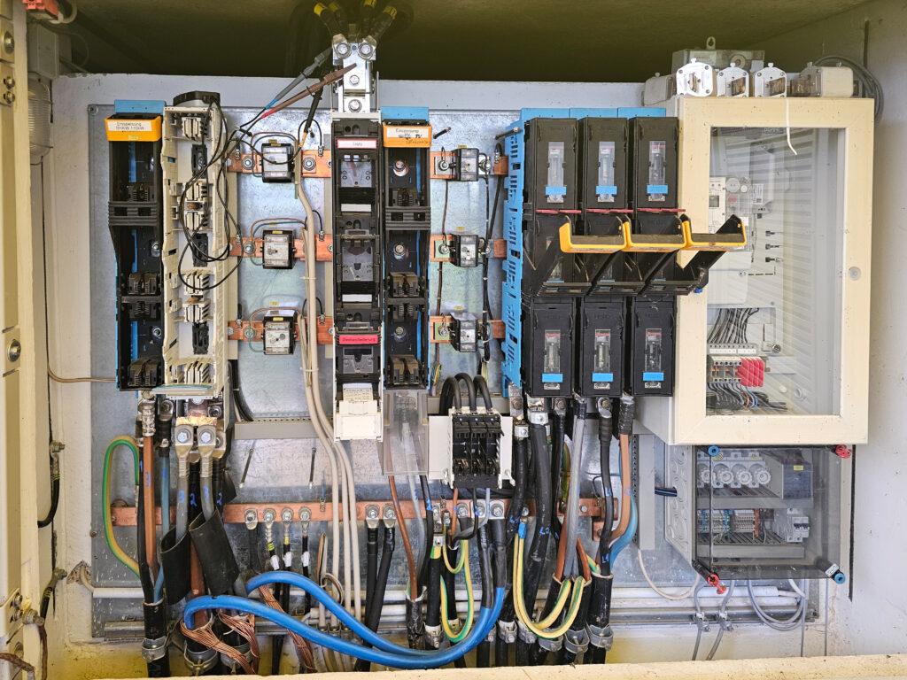 Geöffneter Schaltschrank mit Sicherungsautomaten, Kabeln und elektrischen Steuergeräten.