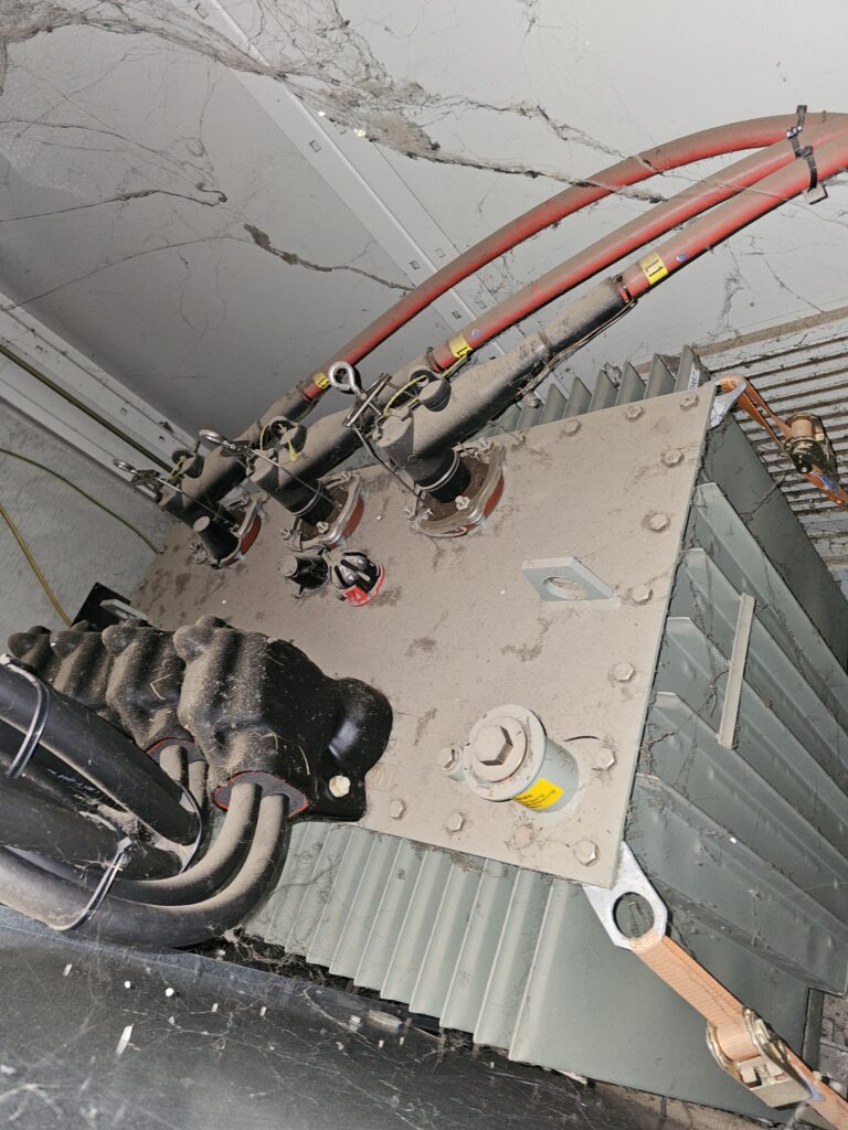 Geöffnete Trafostation mit sichtbaren Leistungsschaltern und Kabelanschlüssen, Gehäuse und Bauteile mit Staub und Schmutz bedeckt.